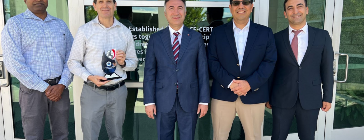 A photo of five men standing in a line outside of the CE-CERT building at UC Riverside. From left to right: Arun Raju, Don Collins (holding a plaque), Prof. İdris Demir, Alfredo Martinez-Morales, and Musa Yilmaz. The photo was taken during Prof. Demir's visit to explore opportunities for international collaboration in energy research and academic exchange.