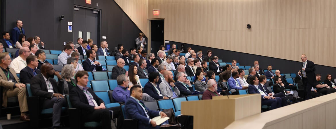 Audience members listen to a presentation in a large lecture hall during the Inaugural Hydrogen Engine Alliance – North America Conference, with keynote speaker Professor Thomas Koch presenting at the front.
