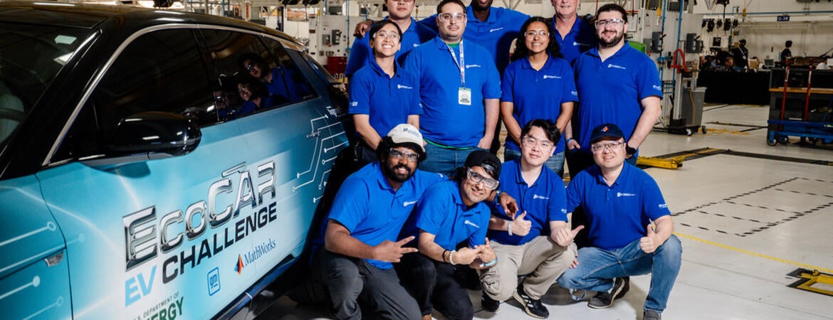 The UCR EcoCAR team gathers for a group photo next to their Cadillac LYRIQ in the workshop, all wearing matching blue team polos and smiling for the camera.