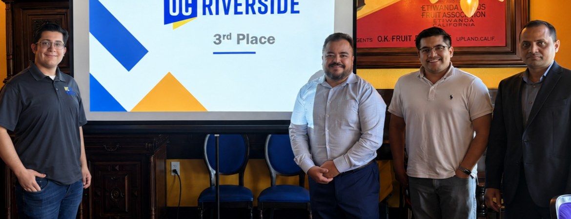 Four individuals stand beside a presentation screen displaying the UC Riverside logo and “3rd Place” during an awards recognition event held in a restaurant banquet room.