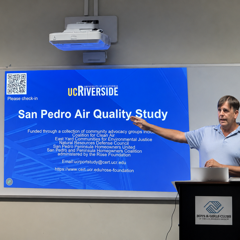 A CE-CERT researcher speaks at a community meeting in San Pedro, standing beside a projected presentation slide titled “San Pedro Air Quality Study.” The meeting was held at the Boys & Girls Club of the Los Angeles Harbor and focused on research examining the impact of ship emissions on local air quality.