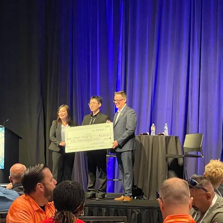 Ziyan Zhang holds a $5,000 scholarship check with two presenters onstage at the 2026 ITS California conference.