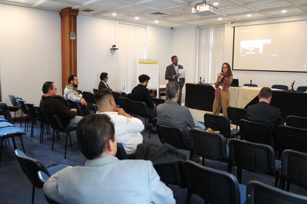 Dr. Arun Raju of CE-CERT and Diana Avalos of AMIVE co-lead a breakout session on infrastructure planning during the Binational Working Group event, speaking to seated attendees in a conference room.