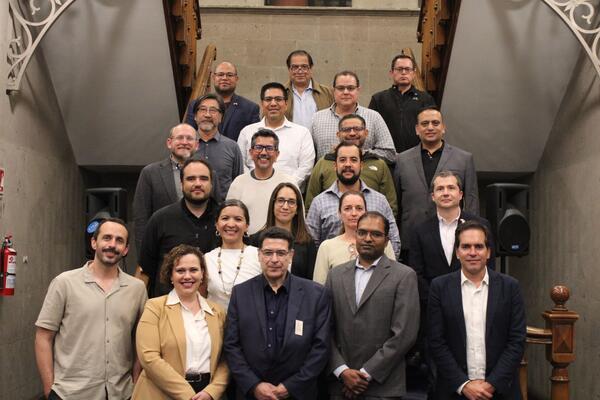 Twenty-two participants from the Binational Working Group on Zero-Emission Vehicles pose on a staircase at the Casa de la Universidad de California in Mexico City.