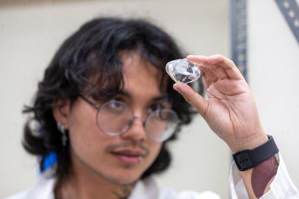Student closely examines a faceted crystal gem to study light scattering effects, specifically Mie scattering phenomena.
