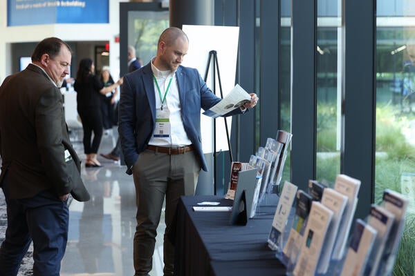 Conference attendee reads a brochure at the sponsor materials table during the Inaugural Hydrogen Engine Alliance – North America Conference, with additional attendees visible in the background.