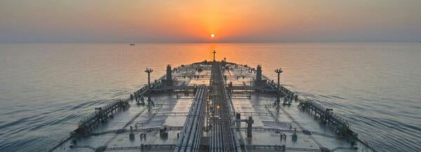 View from the deck of a large cargo vessel at sea during sunset, with pipelines and equipment stretching toward the horizon.