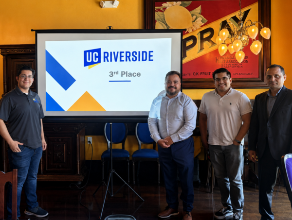 Four individuals stand beside a presentation screen displaying the UC Riverside logo and “3rd Place” during an awards recognition event held in a restaurant banquet room.