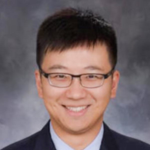 man smiling with glasses and suit in front of gray background