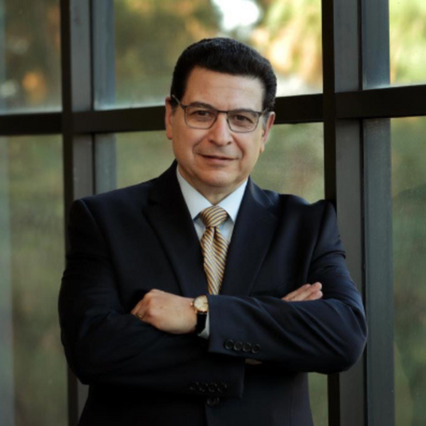 man wearing suit and tie in front of window with short black hair and glasses