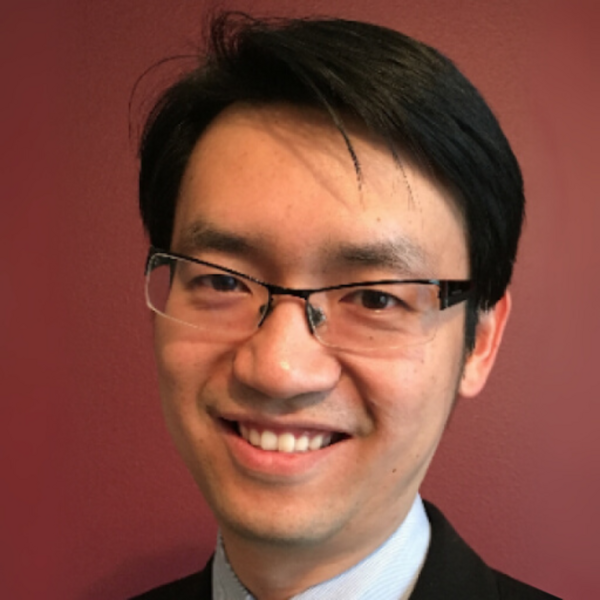 Man with black hair and glasses smiling in front of reddish brown background