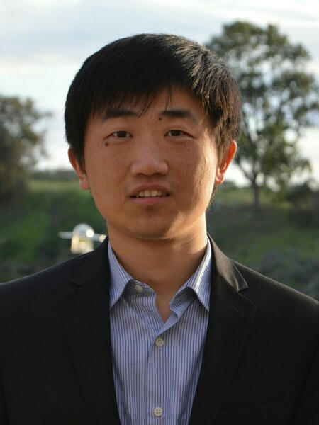 man with blue collared shirt and blazer in front of park background