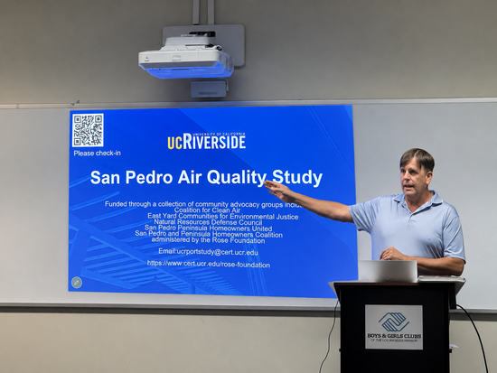 A CE-CERT researcher speaks at a community meeting in San Pedro, standing beside a projected presentation slide titled “San Pedro Air Quality Study.” The meeting was held at the Boys & Girls Club of the Los Angeles Harbor and focused on research examining the impact of ship emissions on local air quality.