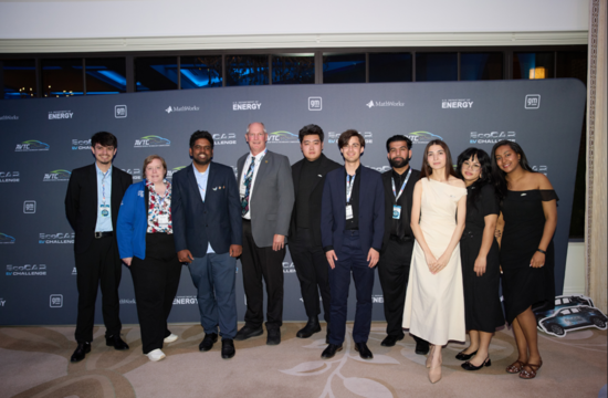 Ten members of the UC Riverside EcoCAR team and faculty advisor pose in front of the EcoCAR EV Challenge backdrop during the final competition awards event in Michigan. The group is dressed in business and formal attire while standing together for a team photo at the closing ceremony.